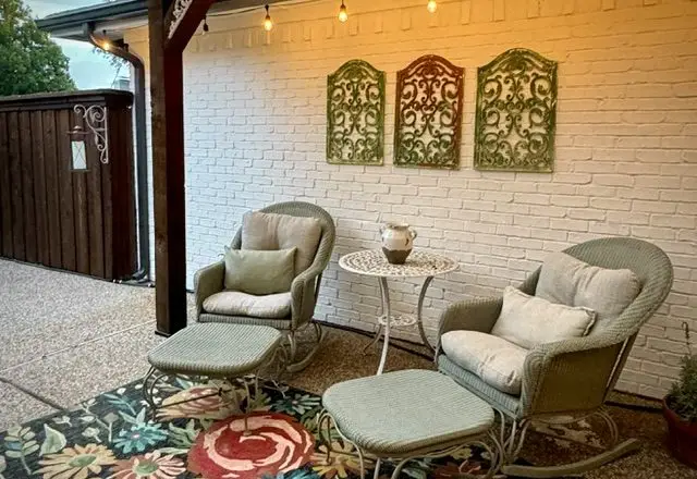 Cushioned rocking chairs and ottomans under the pergola, strung with lights