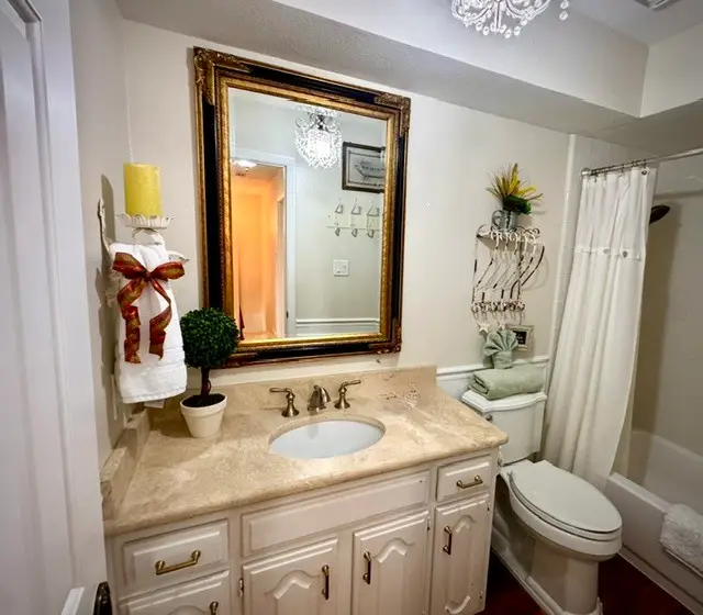 Full bathroom with a crystal chandelier, gold-framed mirror and tub-shower