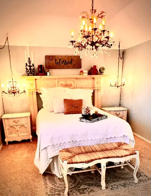 Primary bedroom glowing under a hand-restored crystal chandelier with a vintage mantel headboard