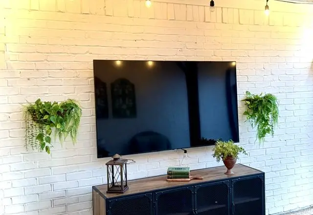 The outdoor television on the white brick wall of the covered patio