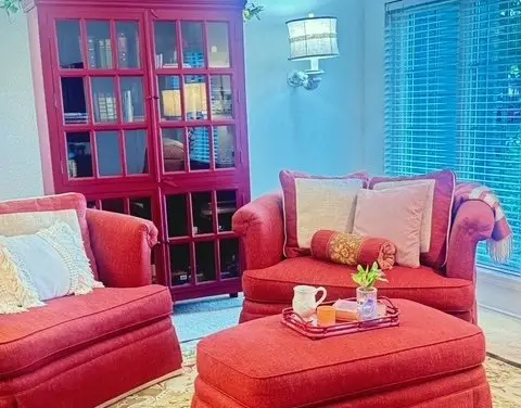 Red loveseats and ottoman beside the antique bookcase in the living room